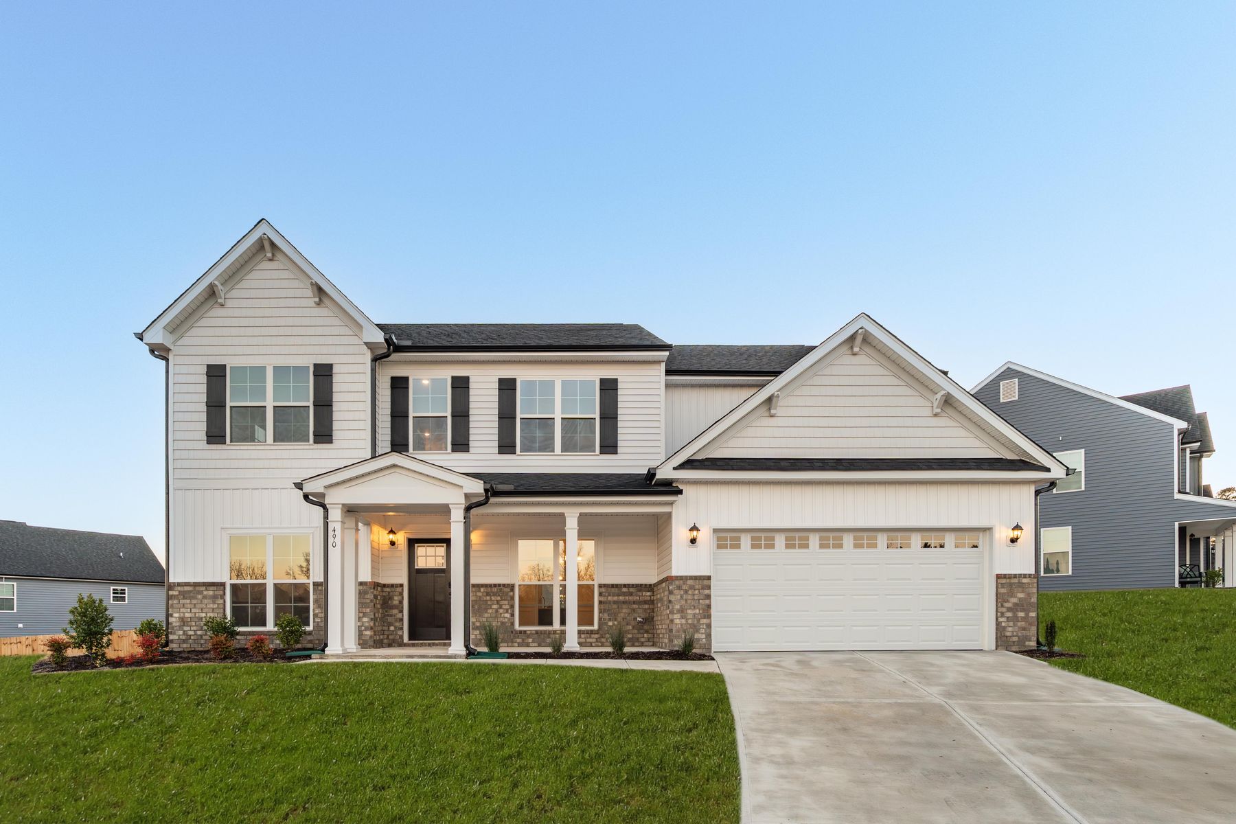Newer two-story suburban home with white siding, brick accents, black shutters, and a two-car garage
